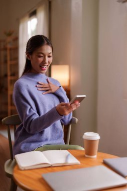 Asyalı kadın akıllı telefon içerikli ev konforlu atmosfer dijital iletişimi ev içi rahat yaşam tarzına neşe ile tepki veriyor.