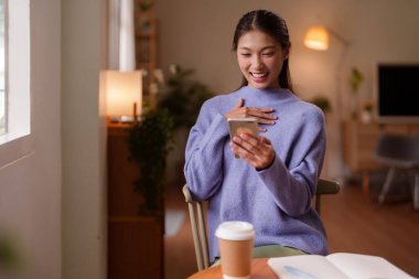 Mutlu genç Asyalı kadın evde telefonla iletişim kuruyor dijital etkileşimin keyfini çıkarıyor modern yaşam tarzı deneyimini kurarken rahat oluyor.