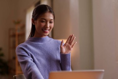 Asyalı bir kadın, evdeki bilgisayarını kullanarak internet üzerinden sorunsuz iletişim kurmak için sanal toplantıya memnuniyetle katılıyor.