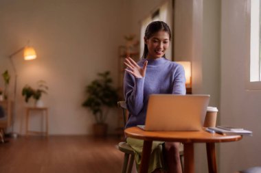 Gülümseyen genç Asyalı kadın rahat bir ev ortamından sanal bir toplantı izliyor. Dizüstü bilgisayar dijital bağlantı tele çalışma yaşam tarzını kolaylaştırır.