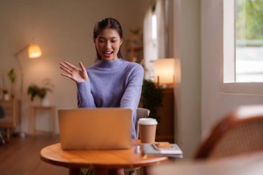 Neşeli Asyalı genç yetişkin kadın bilgisayarında konuşuyor. Ev ofisinden uzak çalışma tarzını temsil eden sanal bir toplantı.