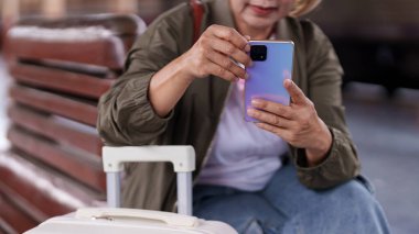 Asyalı yaşlı gezgin iletişim kontrol programı ve yolculuk detayları planlama teknolojisi için akıllı telefon kullanarak tren platformunu bekliyor.