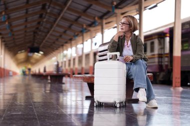 Asyalı son sınıf yolcusu elinde telefon çantası olan bankta dinleniyor ve yolculuk macerasını bekliyor.