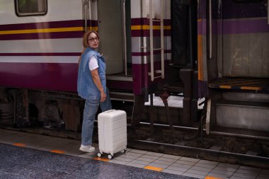 Kıdemli Asyalı kadın tren istasyonu hazır seyahat için beyaz bavul bir sonraki vagon toplu taşıma yolculuğu macera yolculuğu
