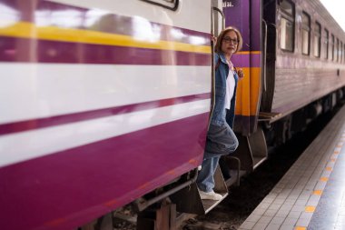 Asyalı son sınıf öğrencisi kadın, tren istasyonu macera platformunda toplu taşımanın keyfini çıkarmaya hazır.