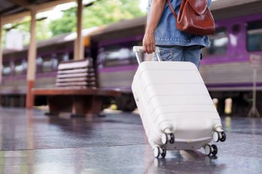 Asyalı biri, tren istasyonunda seyahat için bavulu çekiyor. Yolculuğa çıkmaya hazır..