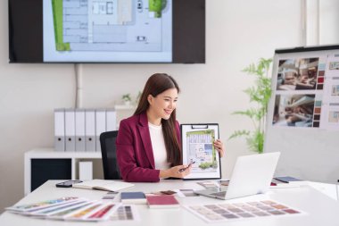 Kendine güvenen Asyalı mimar kadın emlakçı ev planlarını açıklıyor. Ofiste ev alıcıları için profesyonel gayrimenkul satış sunumu.