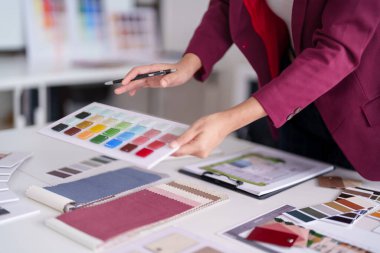 Profesyonel yetişkin Asyalı tasarımcı, mimari ev dekorasyonu projeleri için renk seçimlerini ve kumaş örneklerini inceliyor. Modern bir stüdyoda yaratıcı planlama.