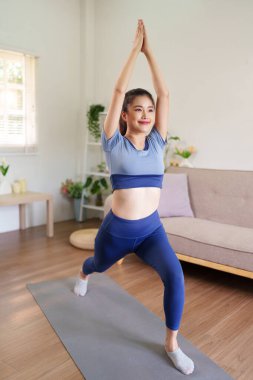 Asyalı yetişkin kadın aydınlık oturma odasında yoga yapıyor. Sağlıklı yaşam tarzının esnekliğinden zevk alıyor. Sıhhatli aktif zindelik.