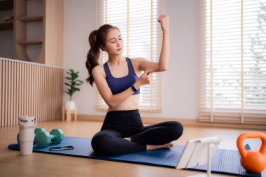 Yetişkin Asyalı kadın evde spor yapıyor. Antrenman sırasında pazılarını ve trisepslerini inceliyor. Sağlıklı olmayı teşvik eder.