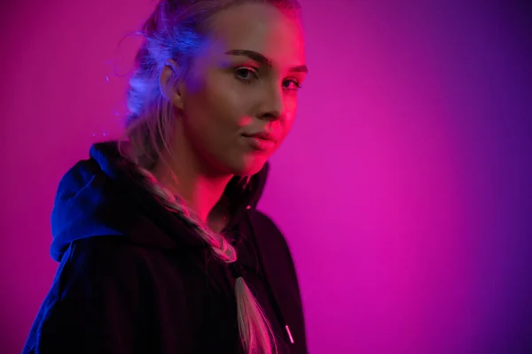 Dark Colorful low-key portrait of a cool and confident blonde woman in hoodie. Red and blue color studio light portrait.