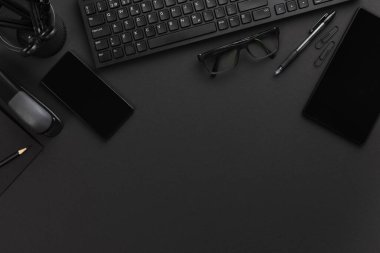 Ofis masasının tam üstünde malzeme, akıllı telefon, tablet, gözlük ve bilgisayar klavyesi gri masanın üstünde.