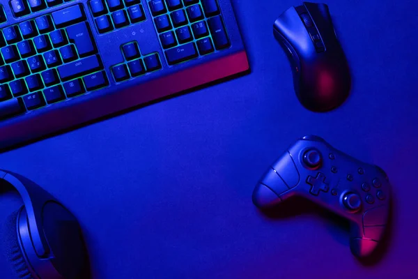 游戏控制器和鼠标在蓝色发光的黑色桌子下面带耳机的绿色发光键盘正上方的视图 当代游戏桌面概念 — 图库照片