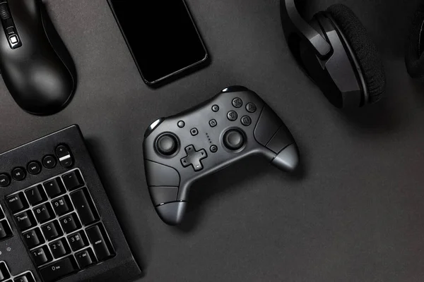 游戏控制器与键盘 耳机和手机等小工具在黑色游戏玩家桌上的俯视图 — 图库照片