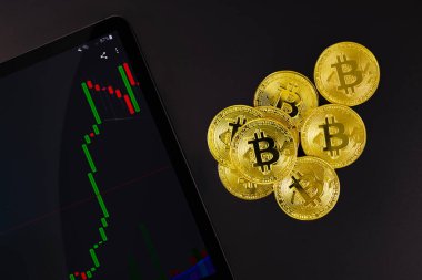 Bitcoin 'in dijital tabletle yukarıdan görünüşü ve çeşitli kripto paralarla boğa grafiği. Durgunlukta hedge olarak BTC