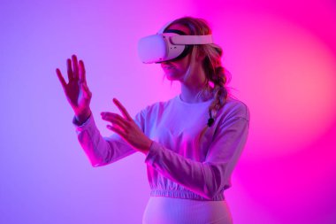 VR kullanarak metaevreni inceliyorum. Sanal gerçeklik kulaklığı takmış, stüdyoda 3 boyutlu oyun oynayan genç bir kadın..