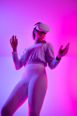VR kullanarak metaevreni keşfeden genç bir kadının düşük açılı görüntüsü. Sanal gerçeklik kulaklığı takıp 3 boyutlu oyun oynayan bir stüdyoda etkileyici bir teknoloji..