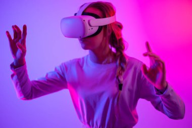 VR kullanarak metaevreni araştırıyorum. Sanal gerçeklik kulaklığı takmış, stüdyoda 3 boyutlu oyun oynayan genç bir kadın..