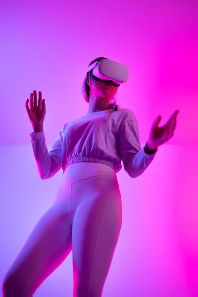 Low angle view of young woman exploring the metaverse using VR. Immersive technology in a studio playing 3D game while wearing a virtual reality headset.