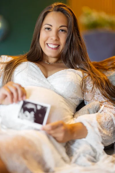 Karnındaki Şişmiş Bebeğin Ultrason Fotoğrafıyla Gülümseyen Hamile Bir Kadın Oturma — Stok fotoğraf