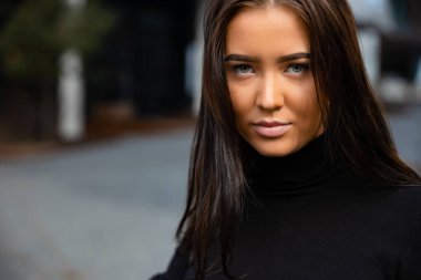 Siyah ceketli çekici bir kadının yakın plan yüz resmi şehirde binaya karşı duruyor..