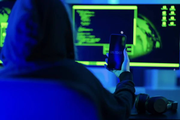 Anonymous mobile cyber security hacker break into and unlock or decrypt cell phone to steal corporate company or private data, identity theft. Hacking in a underground dark green and blue room.