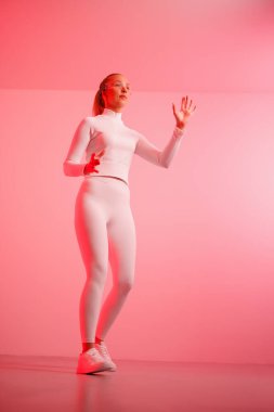 Akıllı gözlüklü genç bayan kırmızı neon arka plana karşı havada el kol hareketi yapıyor.