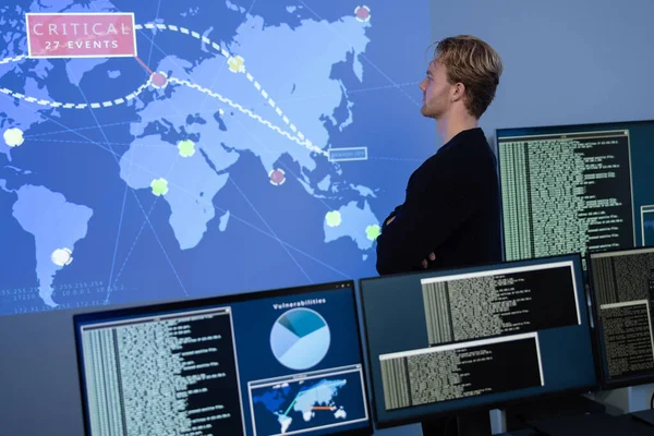 Cyber security analyst in a cyber security operations center SOC. Multiple screens showing map, incident logs and alert data.