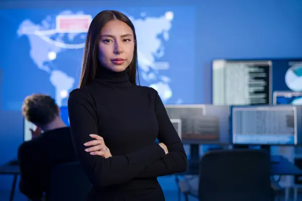 Confident female Cyber Security Analyst or Manager in enterprise Security Operations Center SOC. A team of security operators working in the background with cybersecurity incidents and alerts.