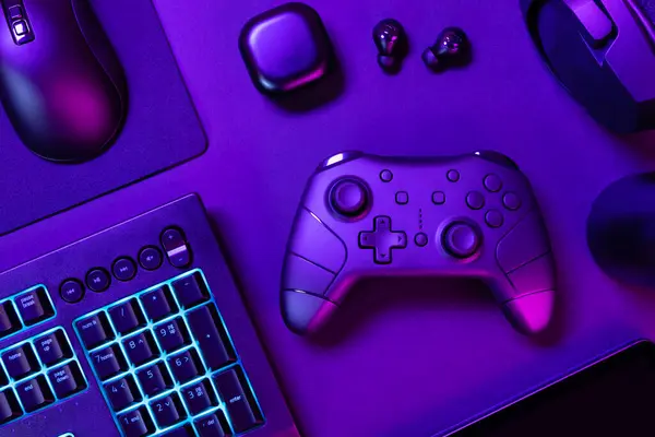 Mor ışıklı ışığın altında, siyah masadaki çeşitli modern cihazların arasında mavi ışıklı klavyenin tam üstünde