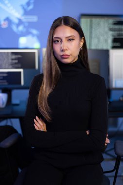 Güvenlik Operasyonları Merkezi SOC 'un kadın Siber Güvenlik Analisti veya yöneticisi. Arka planda siber güvenlik olayları ve alarmlarıyla çalışan bir güvenlik operatörü ekibi.