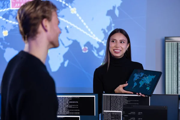 Smiling cyber security team working in a Cyber Security Operations Center SOC. Woman work as Chief Information Security Officer CISO and manager pointing on a real time map om tablet.
