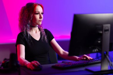 Profesyonel bir bayan oyuncu bilgisayar oyununa odaklanmış renkli ışıklandırma ve modern ekipmanlarla dolu bir odada oynuyor..