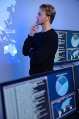 Thoughtful cyber security analyst in a cyber security operations center SOC. Multiple screens showing map, incident logs and alert data. clipart