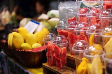 Kalabalık bir Tayland pazarında plastik bardaklarda sunulan renkli taze meyve seçimi Tayland 'daki otantik sokak yemekleri kültürünü popüler bir seyahat merkezi olarak yansıtıyor..