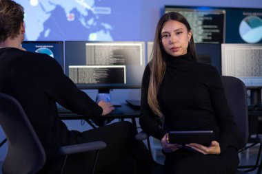 Güvenlik Operasyonları Merkezi SOC 'un kadın Siber Güvenlik Analisti veya yöneticisi. Arka planda siber güvenlik olayları ve alarmlarıyla çalışan bir güvenlik operatörü ekibi.