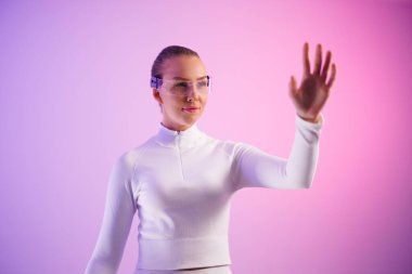 Akıllı gözlük takan genç bir kadın, renkli arka plana işaret ediyor.