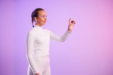 Akıllı gözlük takan genç bir kadın mor arka planda dururken el kol hareketi yapıyor.