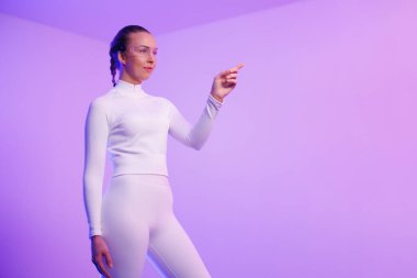 Akıllı gözlük takan genç bir kadın neon rengi mor arka plana işaret ediyor.