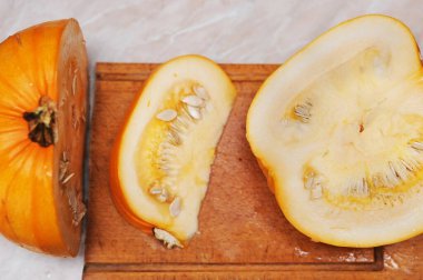 Sarı balkabağı mutfakta tahta bir tahtanın üzerinde kesilir. Kadın balkabağıyla yulaf lapası pişirecek. Yatay