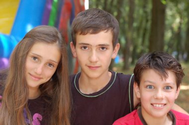 En iyi üç arkadaş - iki erkek ve kız kardeş yazın parkta dinleniyorlar. Çocuklar mutlu ve gülümsüyor, aralarında iki genç var. Yaz zamanı.