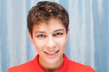 Dişlerinde diş telleri olan koyu renk saçlı yakışıklı bir çocuk güzel gülümsüyor. Diş sağlığı konsepti