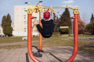 Küçük çocuk güçlü ve sağlıklı bir şekilde büyümek istiyor bu yüzden sokakta yatay barlarda takılıyor ve yukarı çekmeyi öğreniyor. Çocuklar için fiziksel aktivite ve sağlık kavramı. Arka görünüm