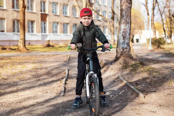 İlkbaharın başlarında, genç bir çocuk okulun yanında bisiklet sürüyor, dinlenmek için durdu, bisiklet sürmeyi öğrendiğine memnun, mutlu bir görünümü var. Çocuğun dikkat çekici kırmızı bir şapkası vardı.
