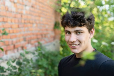 Parkta mutlu bir şekilde gülümseyen genç adam, koyu saçlı ve güzel bir gülüşü olan genç bir adamın yakın portresi, gizemli bir yüzü var, hayatındaki bir şey için heyecanlı.