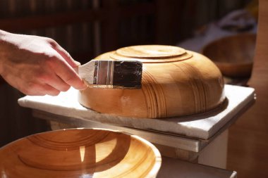 Delikanlının yeni bir hobisi var. Tabakları tahtadan oyup cilalıyor ve ailesine ve arkadaşlarına veriyor. Adam ahşap tabakları fırçayla cilalıyor. Seçici odak