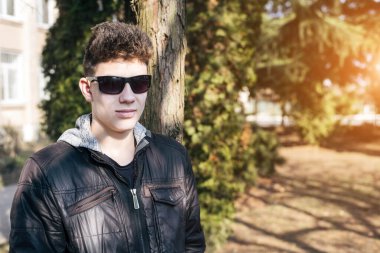 Güneşli bahar havasında güneş gözlüklü güzel bir genç sokakta spor yaptıktan sonra ağacın yanında dinleniyor. Adam güneş gözlüğü takmak için gözlerini ayırmıyor.