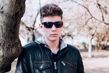 Ergenlik çağında gözlüklü bir çocuk baharda ağacın yanında duruyor ve üzgün. Çocuğun kötü bir ruh hali var çünkü ailesiyle kavga etti.