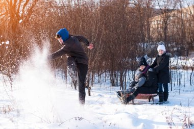 Aile birlikte eğleniyor. Kışın karda kızaklara biniyorlar. En büyük oğul kızaklara biniyor anne, kız kardeş, erkek kardeş ve babaları onların fotoğraflarını çekiyor.