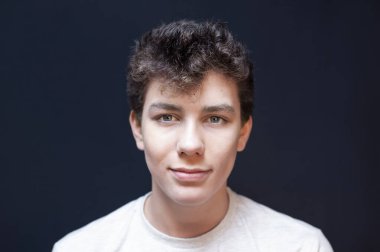 Siyah arka planda koyu saçlı, samimi bir gülümsemeyle genç bir çocuğun portresi. Bir gencin kıvırcık saçları ve güzel gözleri vardır.